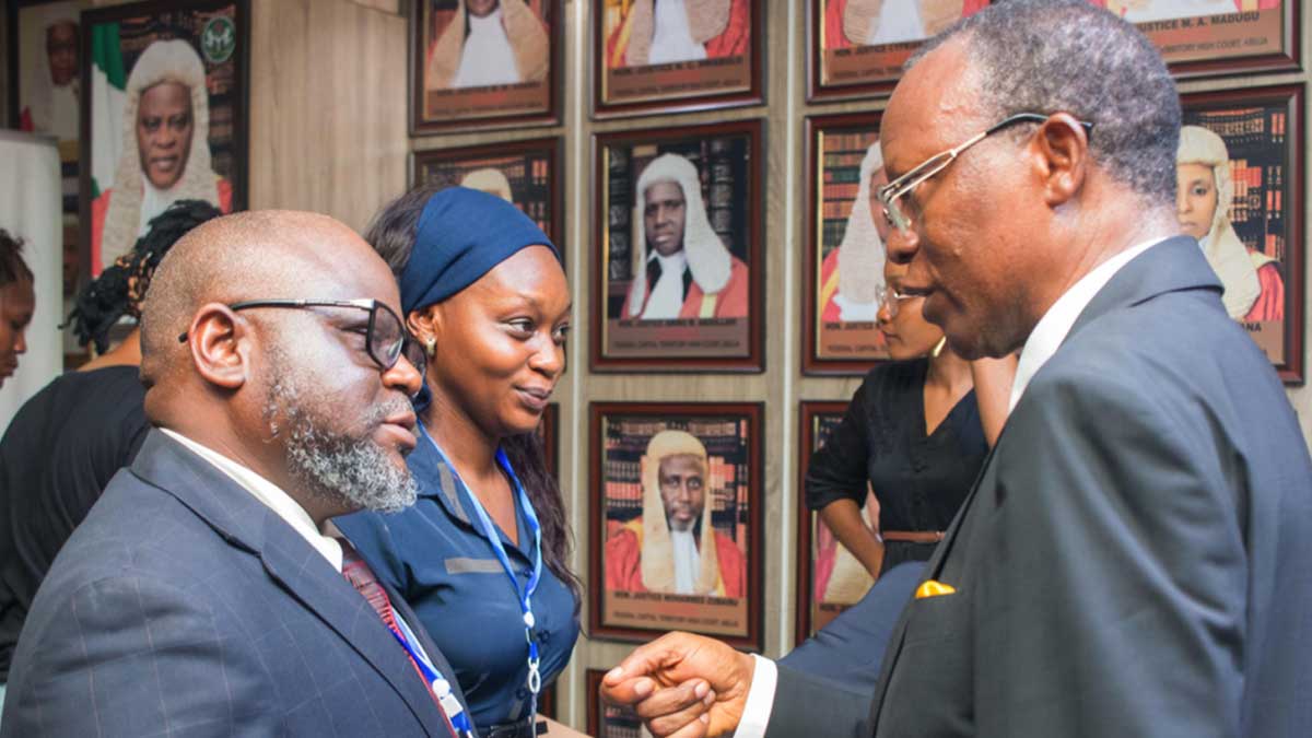 People in conversation in front of a wall with framed portraits of individuals in judicial robes.